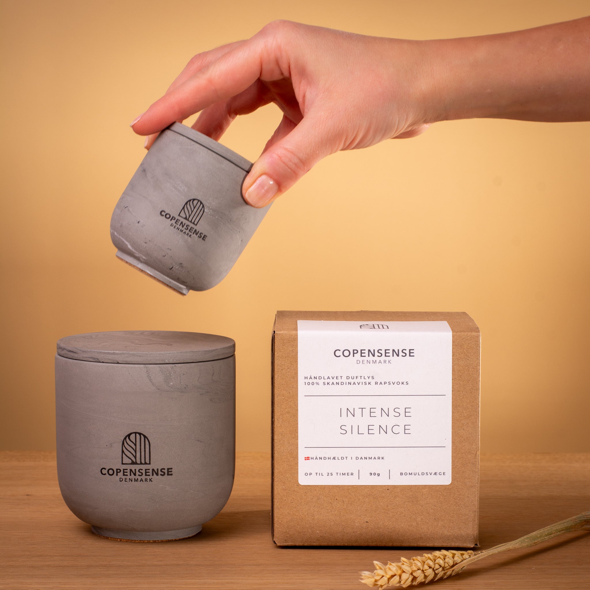 Hand holding mini 90g Intense Silence candle next to large 270g Nordic Slate vessel and minimalist gift box. Size comparison of grey rapeseed wax candles.